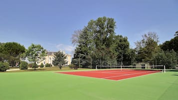 Ein Tennisplatz mit Netz, umgeben von Bäumen und einem Gebäude im Hintergrund.