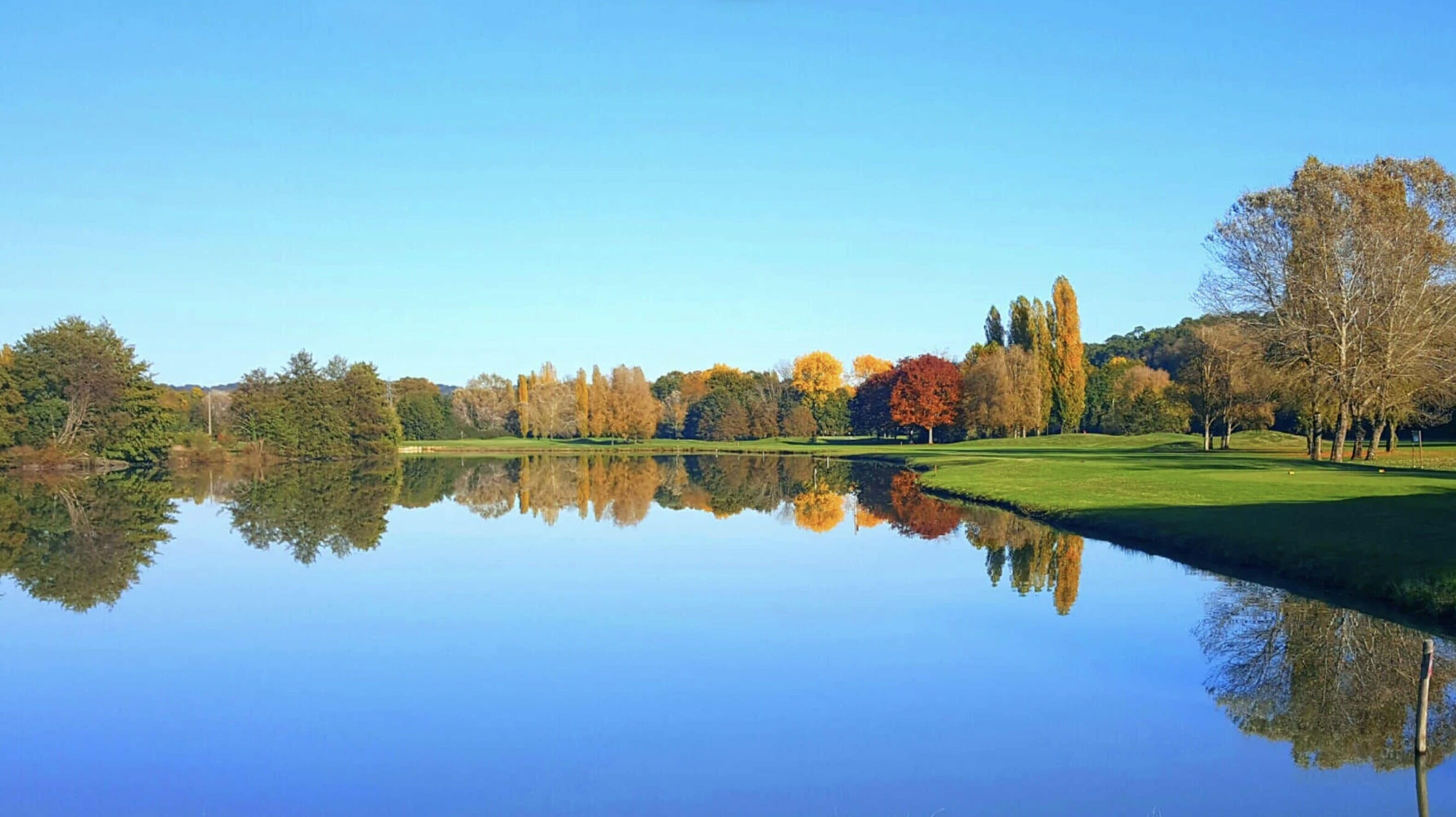 A calm lake reflecting trees and a clear sky.
