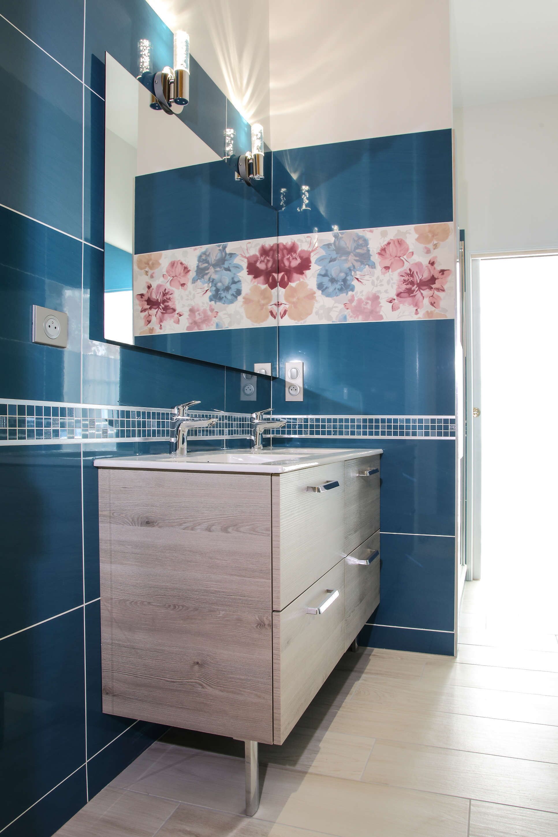 Une salle de bain moderne avec un meuble-lavabo en bois, un grand miroir et un pare-feu en carreaux à motifs floraux.