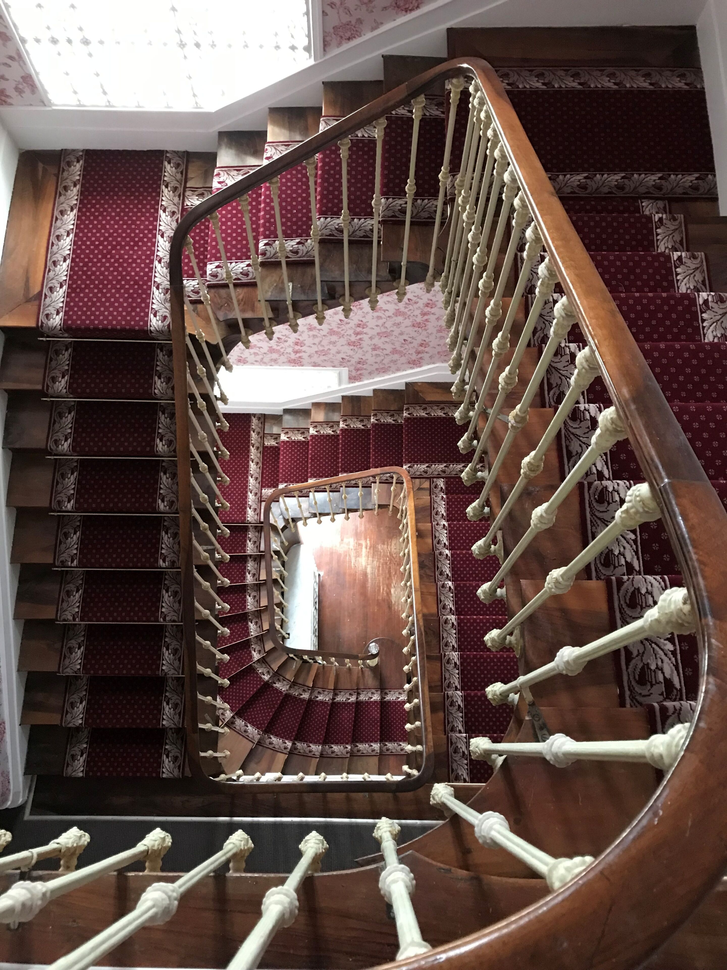 Una imponente escalera con barandilla de madera y piso cubierto de alfombra roja.