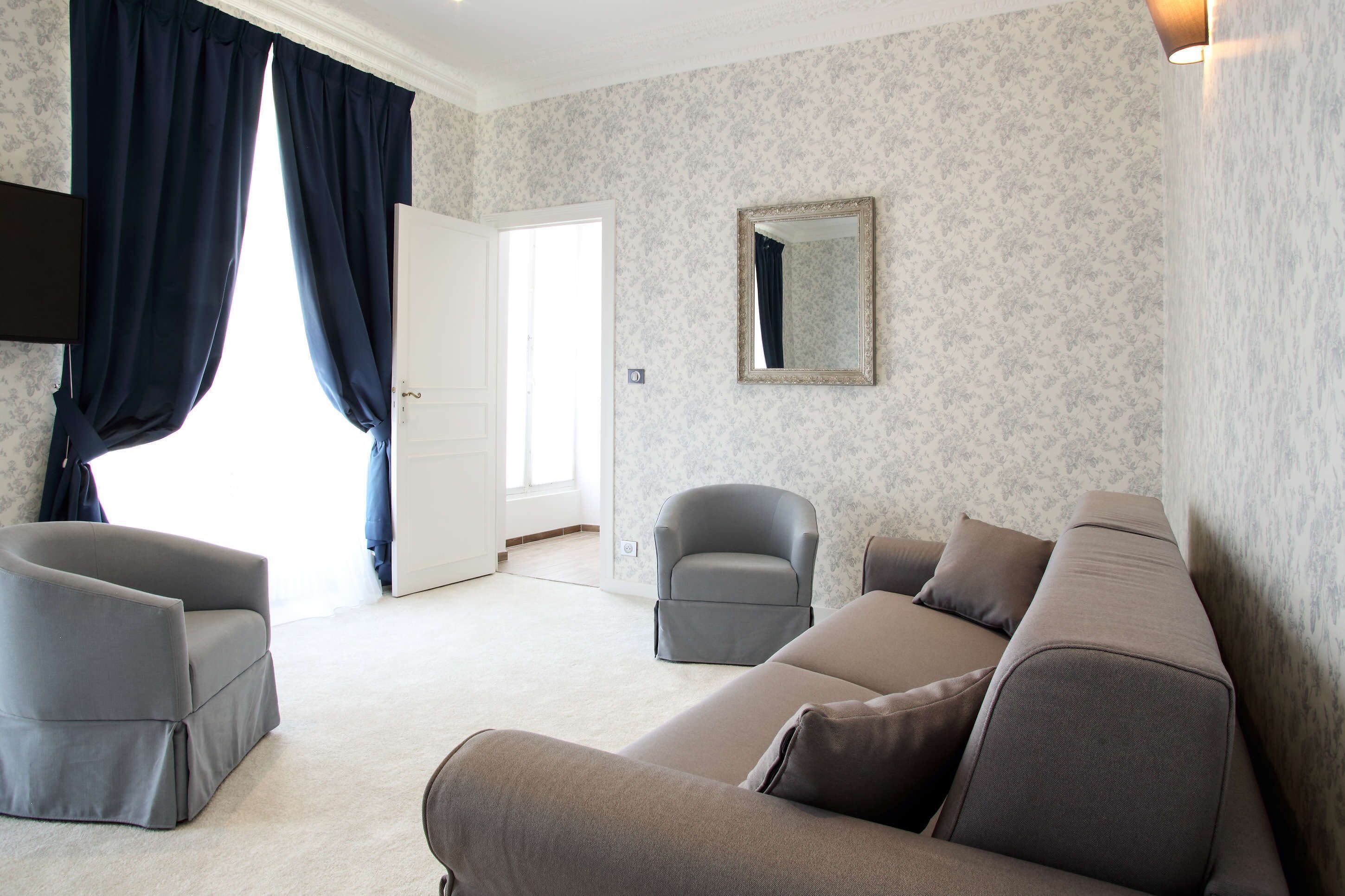 Una sala de estar moderna con un sofá gris, un sillón gris y un sillón pequeño. Una puerta da a otra habitación y un espejo cuelga en la pared.