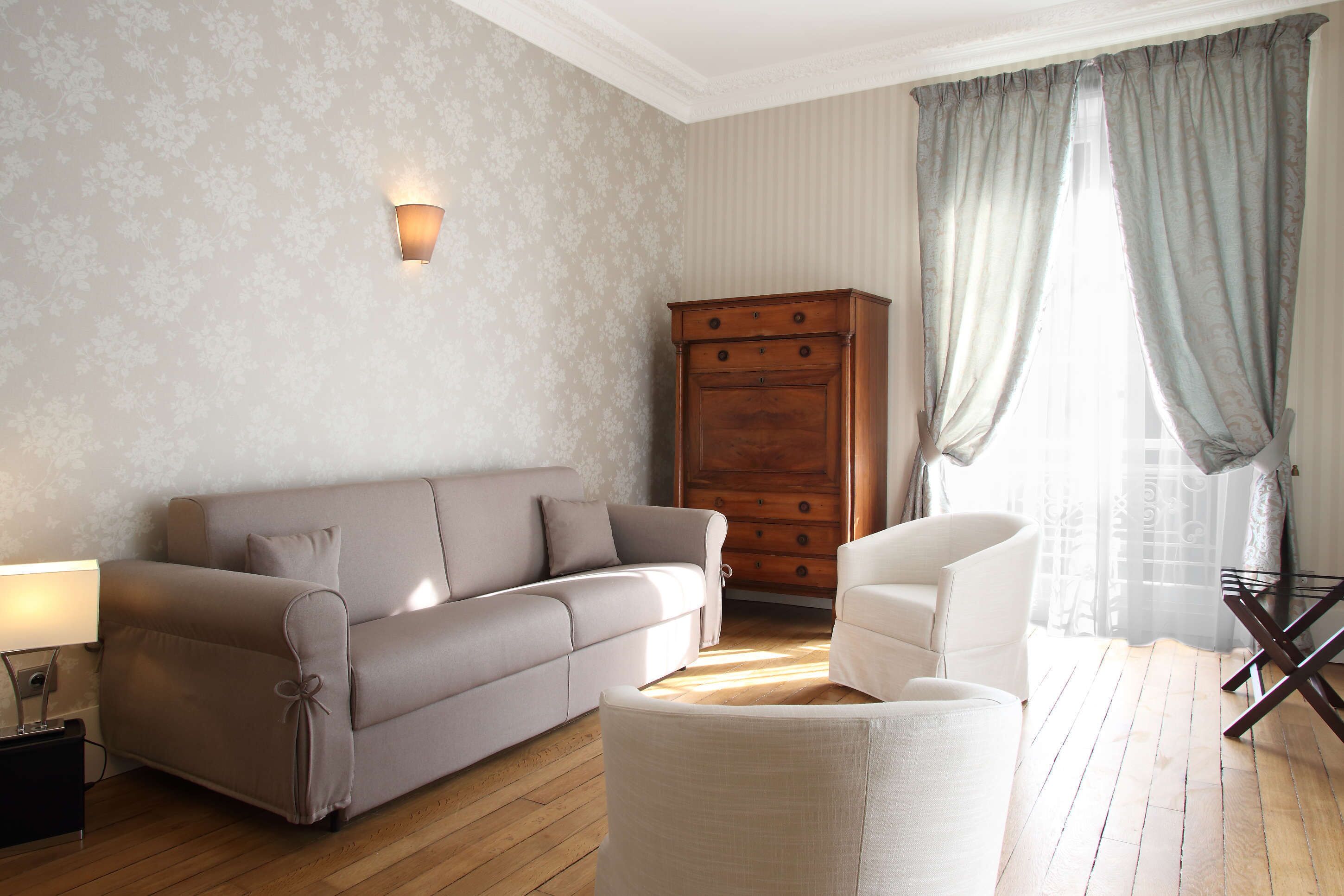 Een woonkamer met een bank, fauteuil, houten kast en een lamp.