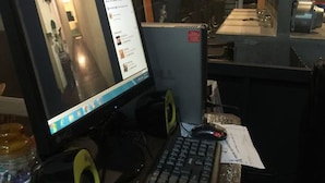 A computer desk with a monitor, keyboard, and speakers in a room with a 'KELUAR' sign on the wall. - Cookoobird Home - Hostel (George Town)