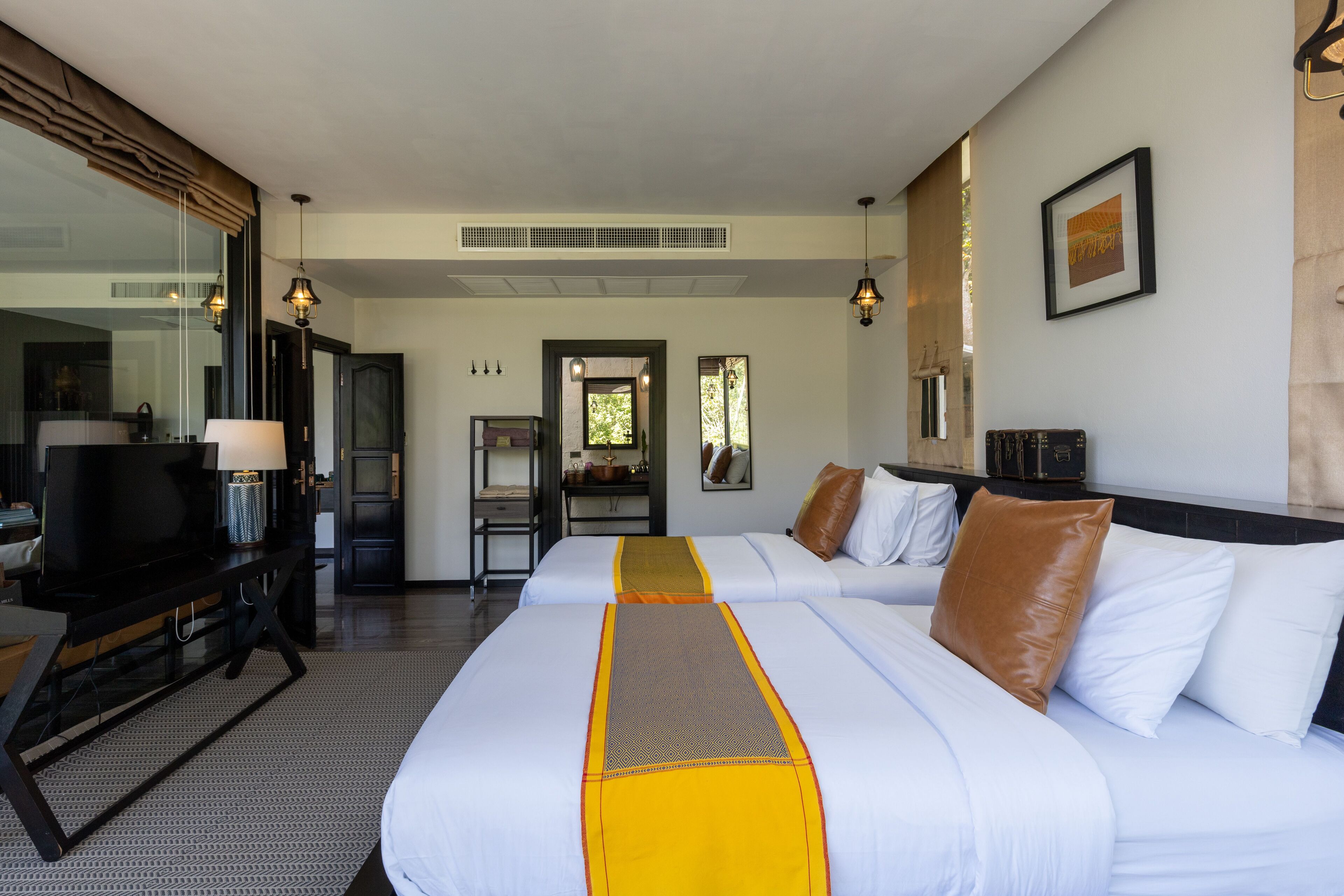 A hotel room with two beds, a desk with a lamp, a television, and a large window.