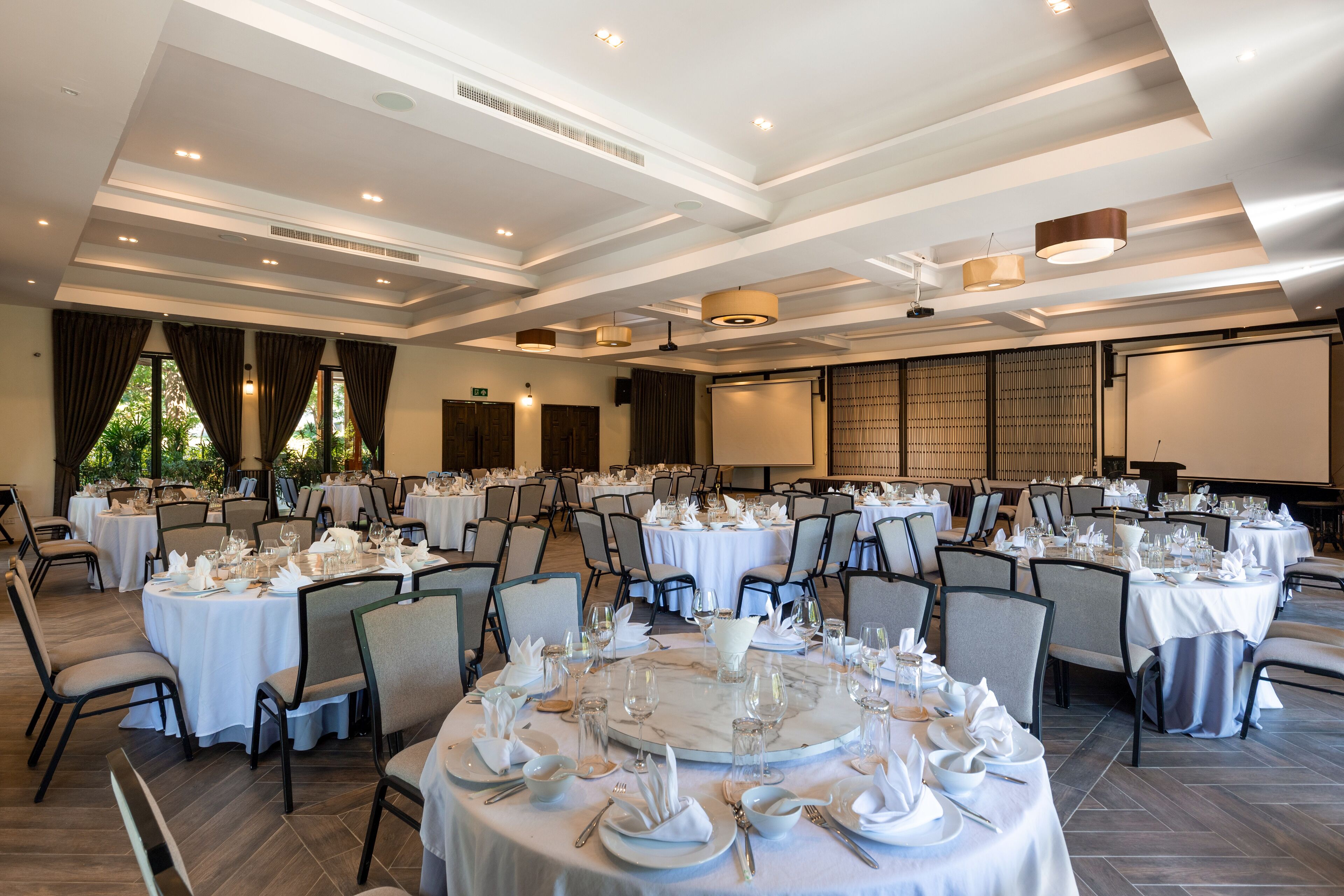 Een balzaal met ronde tafels gedekt voor een formeel evenement, met witte tafellakens, stoelen en servies.