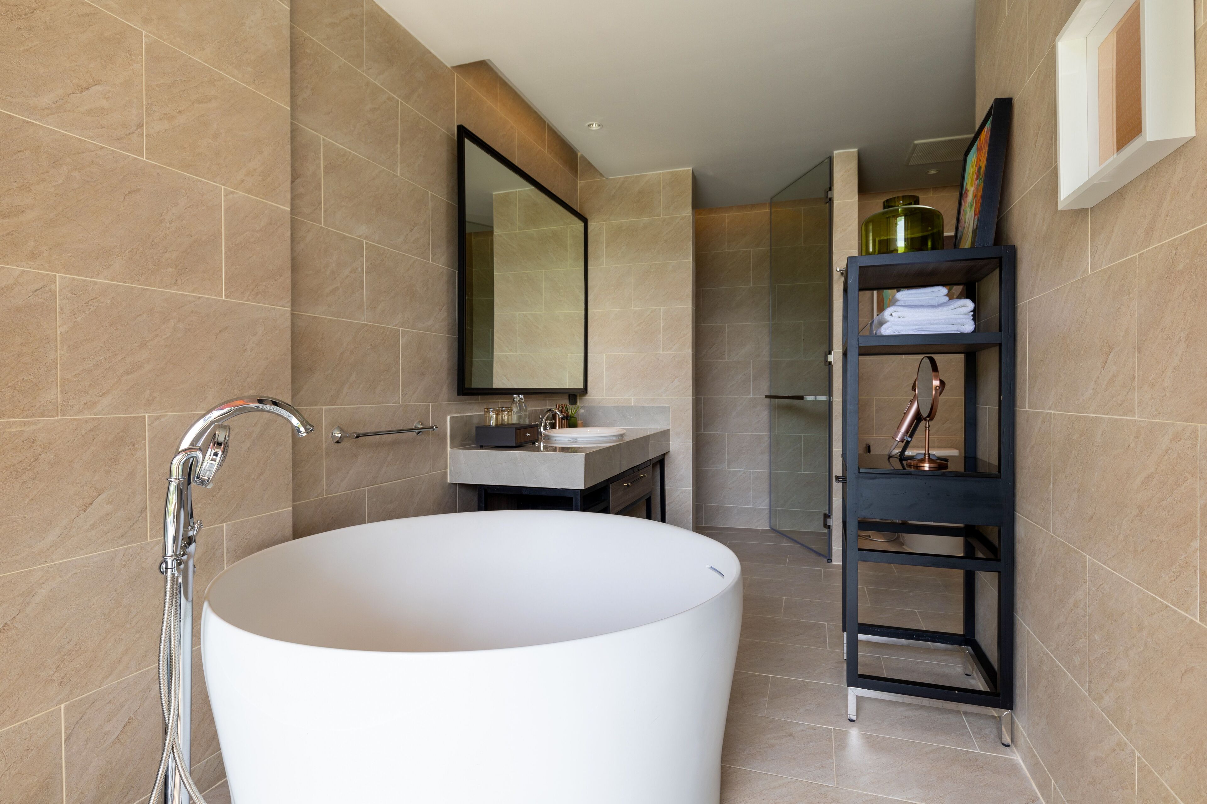 A modern bathroom with a freestanding bathtub, a vanity with a mirror, and a shelf with towels.