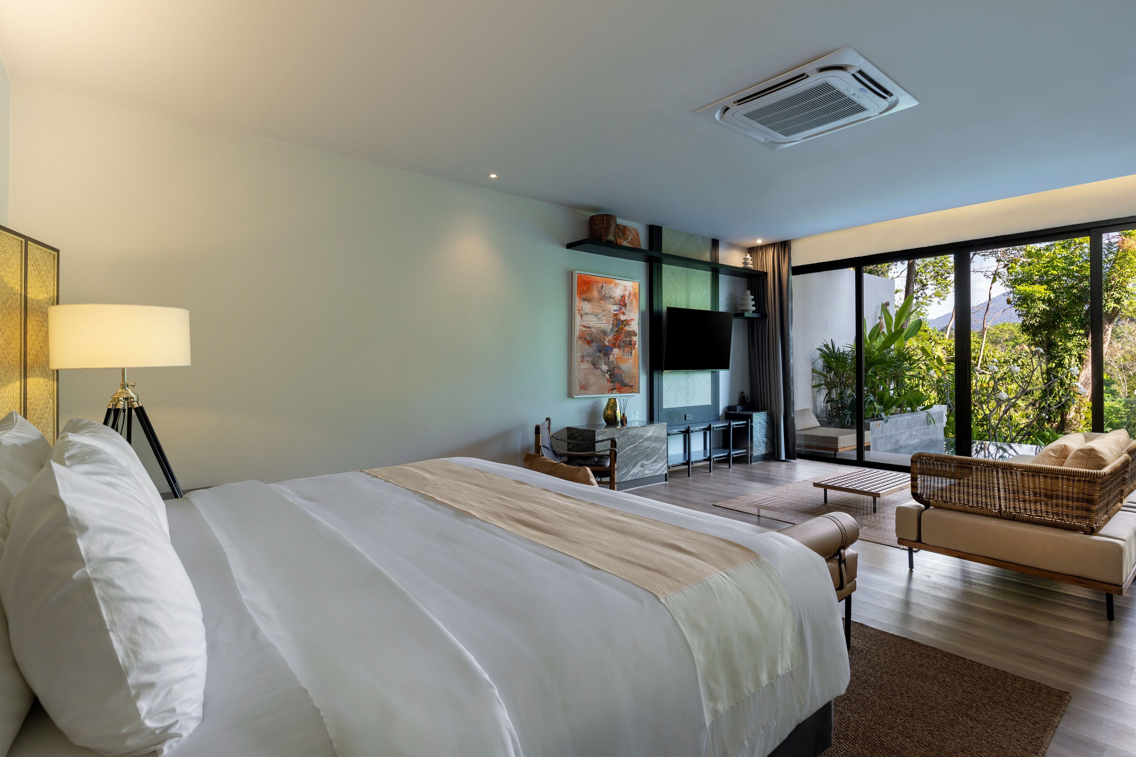 Une chambre d’hôtel moderne dotée d’un grand lit, d’un bureau, d’un canapé et d’un balcon offrant une vue sur la verdure.