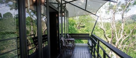 A covered outdoor area with a wooden deck, metal railings, and a table with chairs.