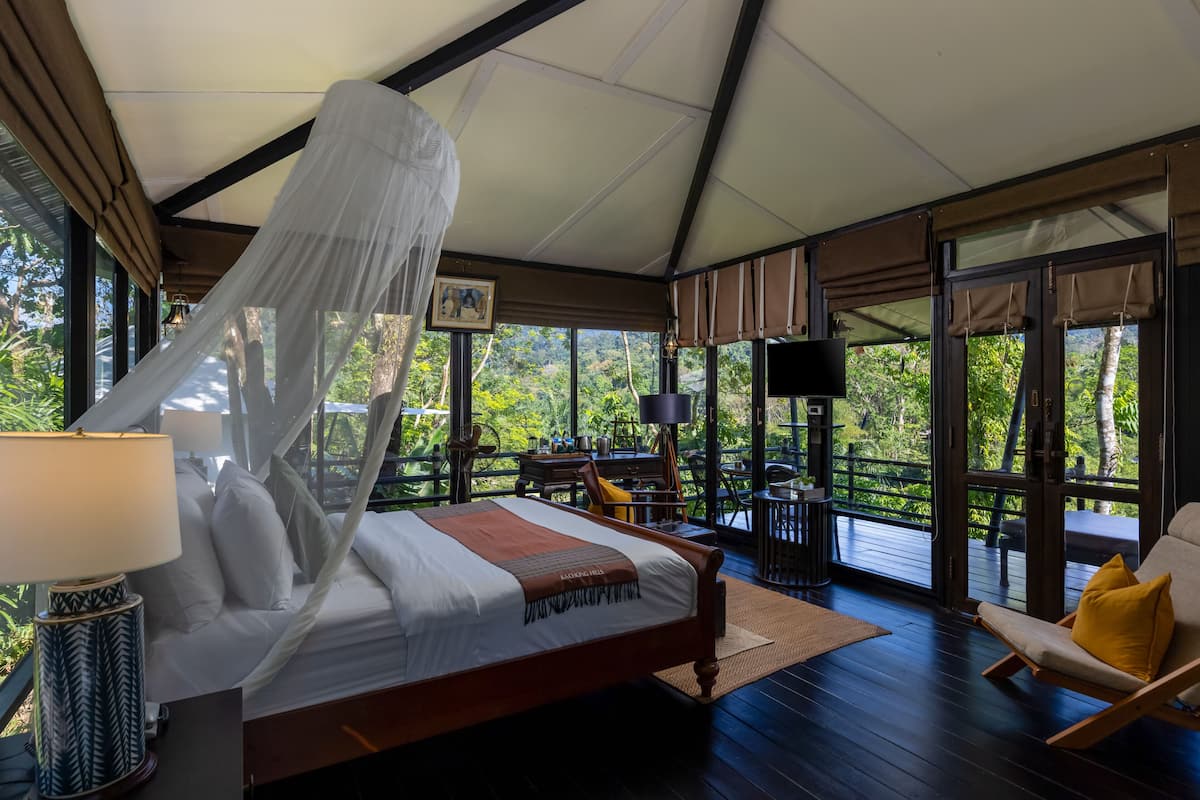 A bedroom with a bed, bedside table, lamp, and a view of the outdoors.