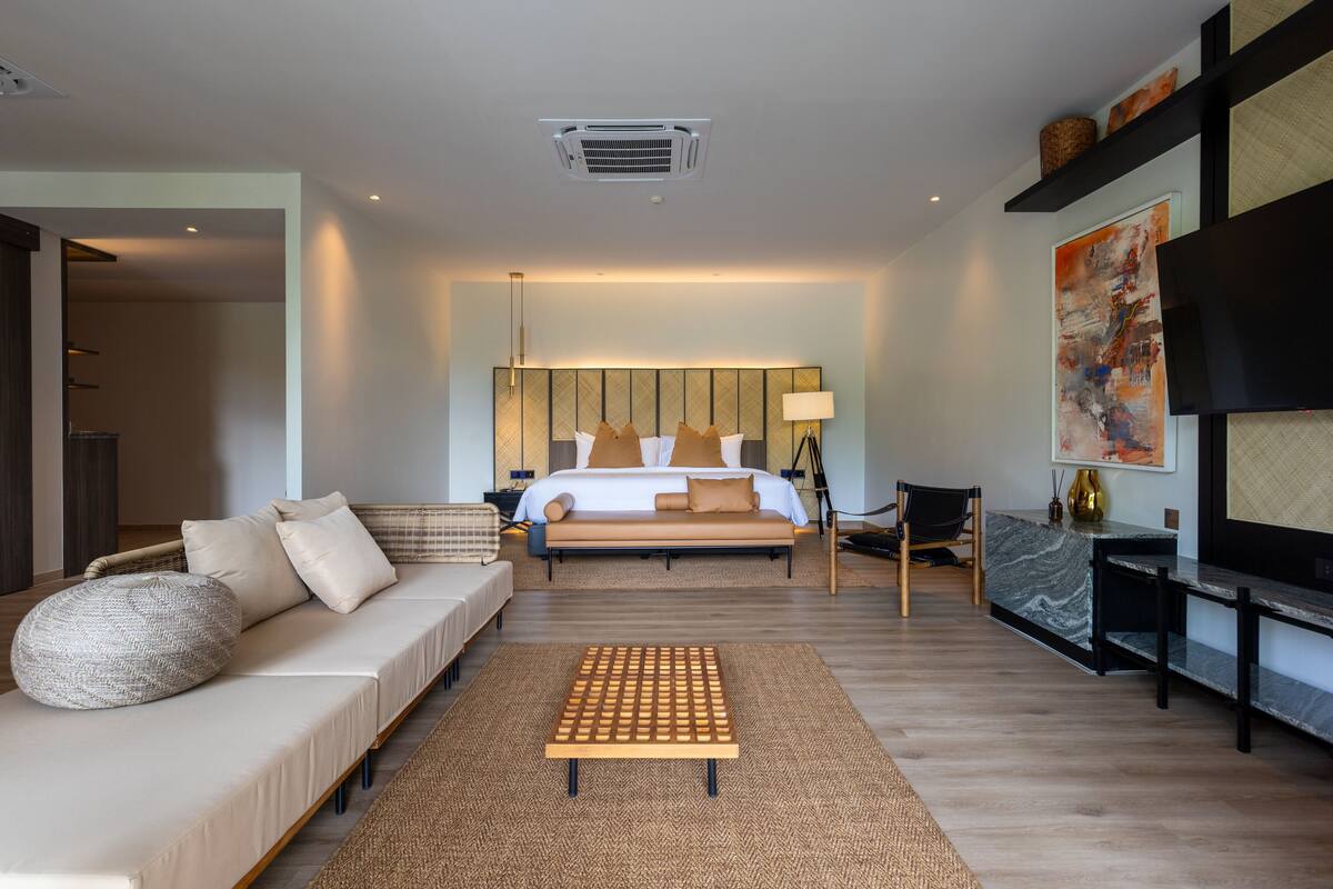 A modern hotel room with a large bed, a sofa, a coffee table, and a TV.
