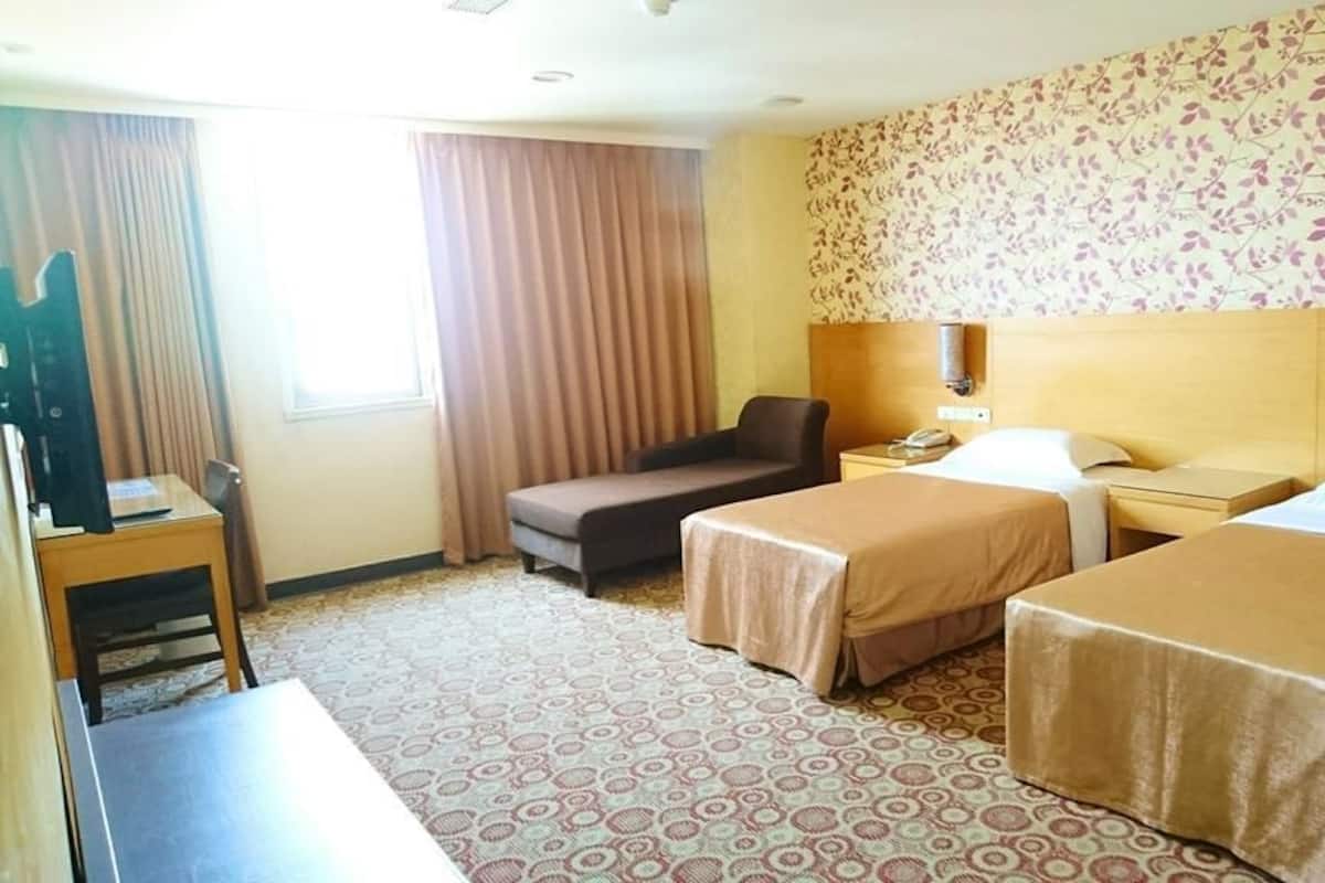 A hotel room with two beds, a desk, a chair, and a small sofa.