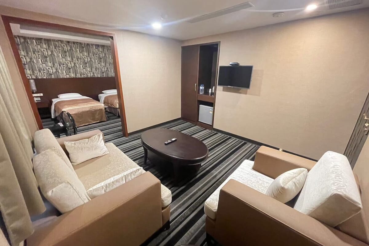 A hotel room with a sofa set, a small round table, a bed, and a television on the wall.