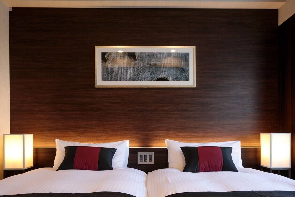 A hotel room with a double bed, two bedside lamps, a framed artwork on the wall, and a wooden headboard.