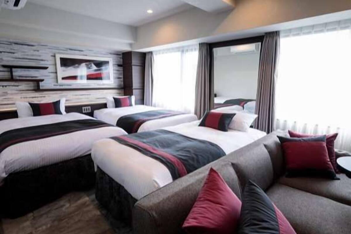 A hotel room with three beds, a sofa, and a large window.