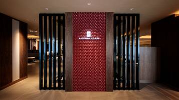 A hotel entrance with a modern design, featuring a red textured wall and vertical wooden slats.
