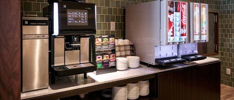 A coffee station with a milk cooler, coffee machines, and beverage dispensers.