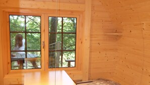 A cabin with two wooden beds, a small table, and a window overlooking greenery.