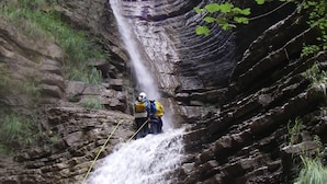 Une personne qui descend en rappel le long d’une cascade rocheuse dans une zone boisée.