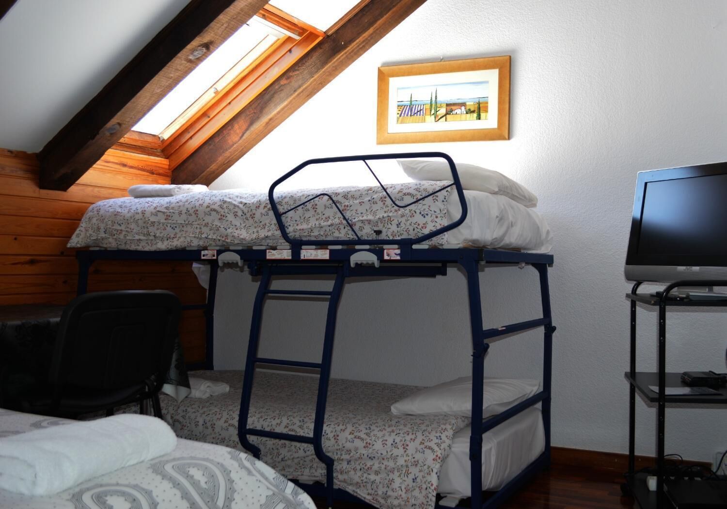 Een stapelbed in een kamer met een schuine plafond, een ingelijst foto aan de muur en een televisie op een standaard.