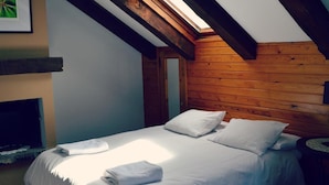 Une chambre avec un plafond en pente, un lambris en bois, un lit avec du linge de lit blanc et un tableau encadré au mur.