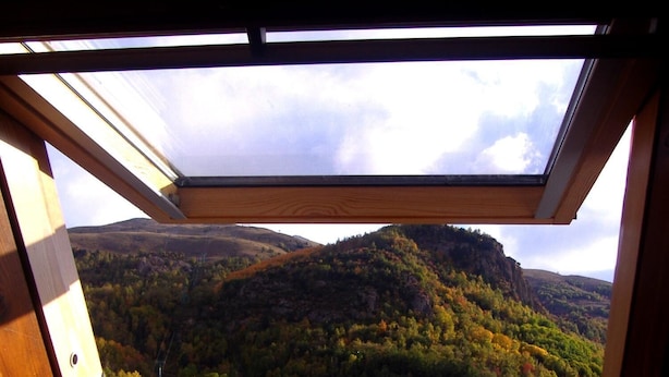 Une lucarne offrant une vue sur un paysage montagneux boisé.