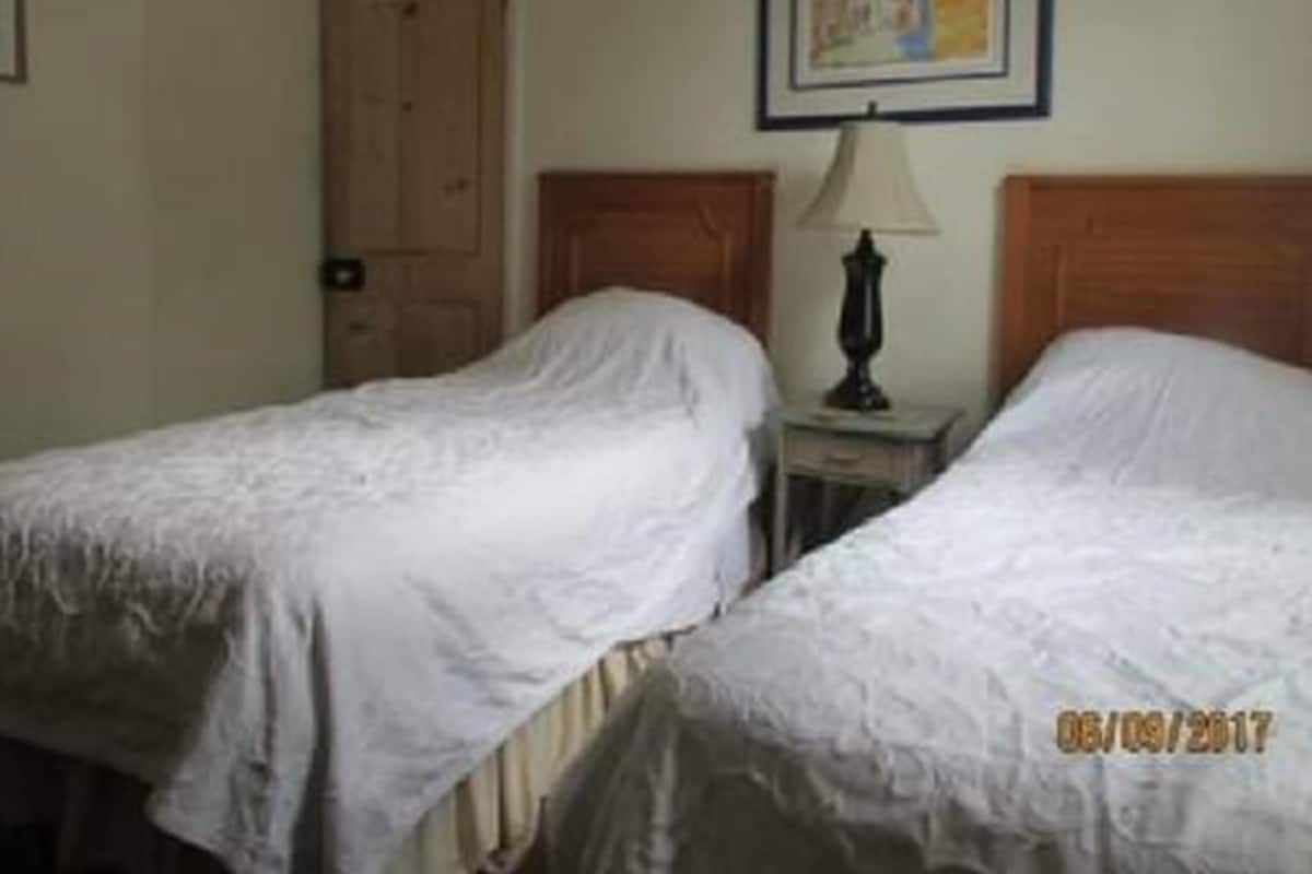 A hotel room with two single beds, a wooden door, a small table with a lamp, and a framed picture on the wall.