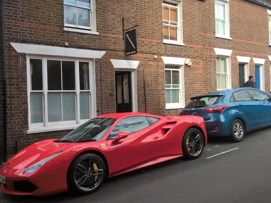 A red sports car parked in front of a brick building with white window frames and a black door.