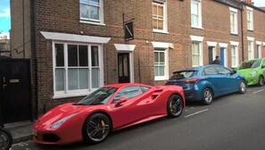 A red sports car parked in front of a brick building with white window frames and a black door.