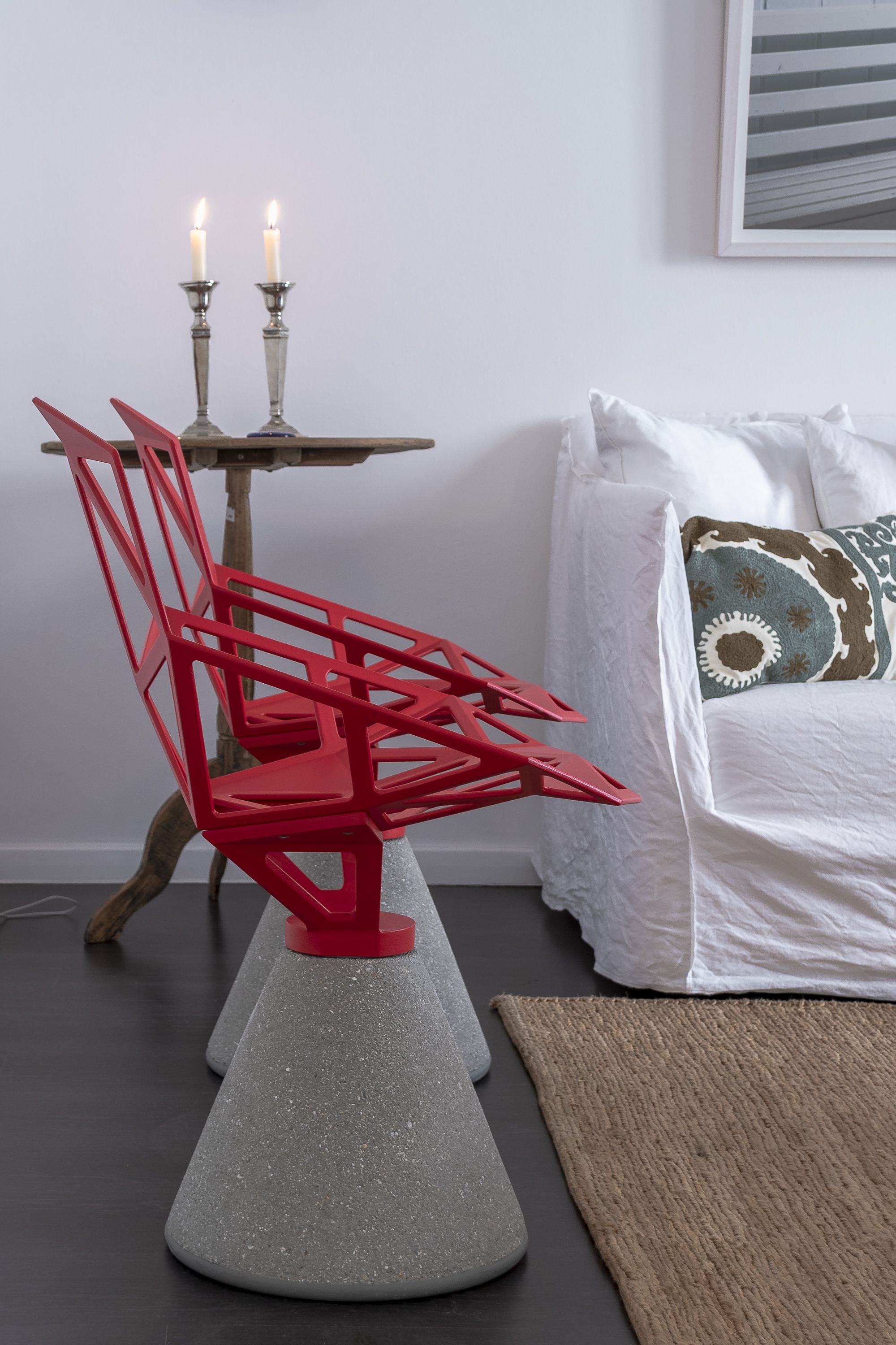 Une pièce avec une chaise rouge, une table avec des bougies et un lit avec un oreiller à motifs.