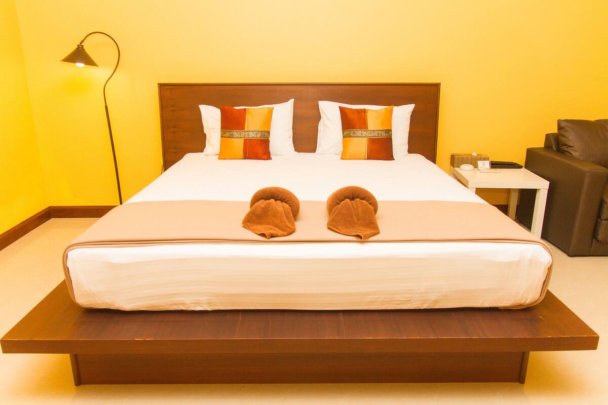 A hotel room with a large bed, two pillows, a bedside table, a lamp, and a chair.