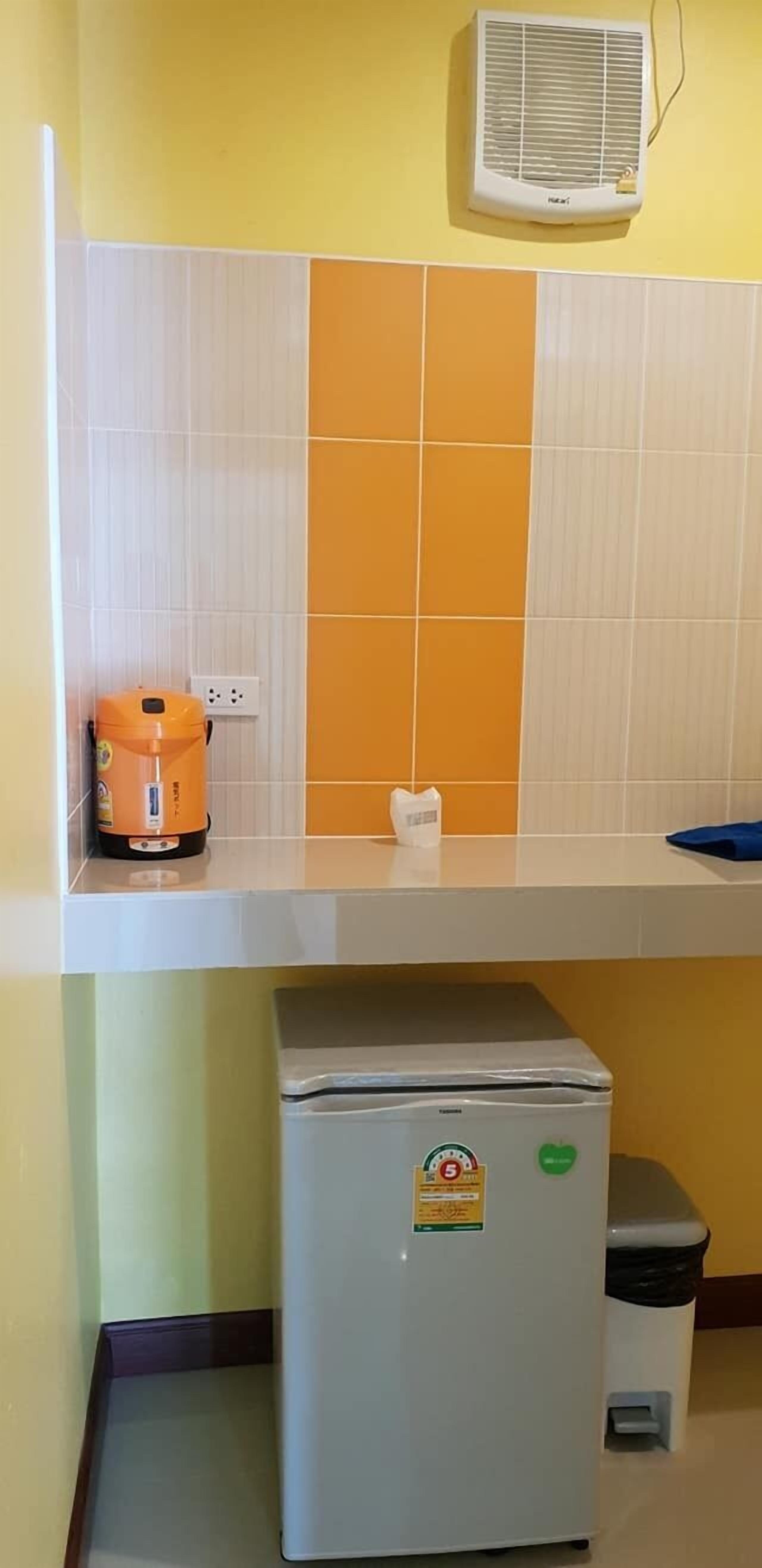 Une cuisine avec un plan de travail blanc, un petit réfrigérateur, un climatiseur fixé au mur et un pare-feu jaune et blanc.