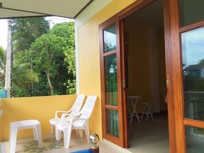 A balcony with two white plastic chairs and a small table, a wooden door, and a view of greenery. - The pearl hometel (Ko Lanta)