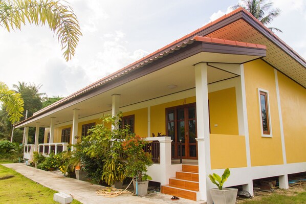 A yellow building with a red roof, a covered porch, and steps leading to the entrance. - The pearl hometel (Ko Lanta)