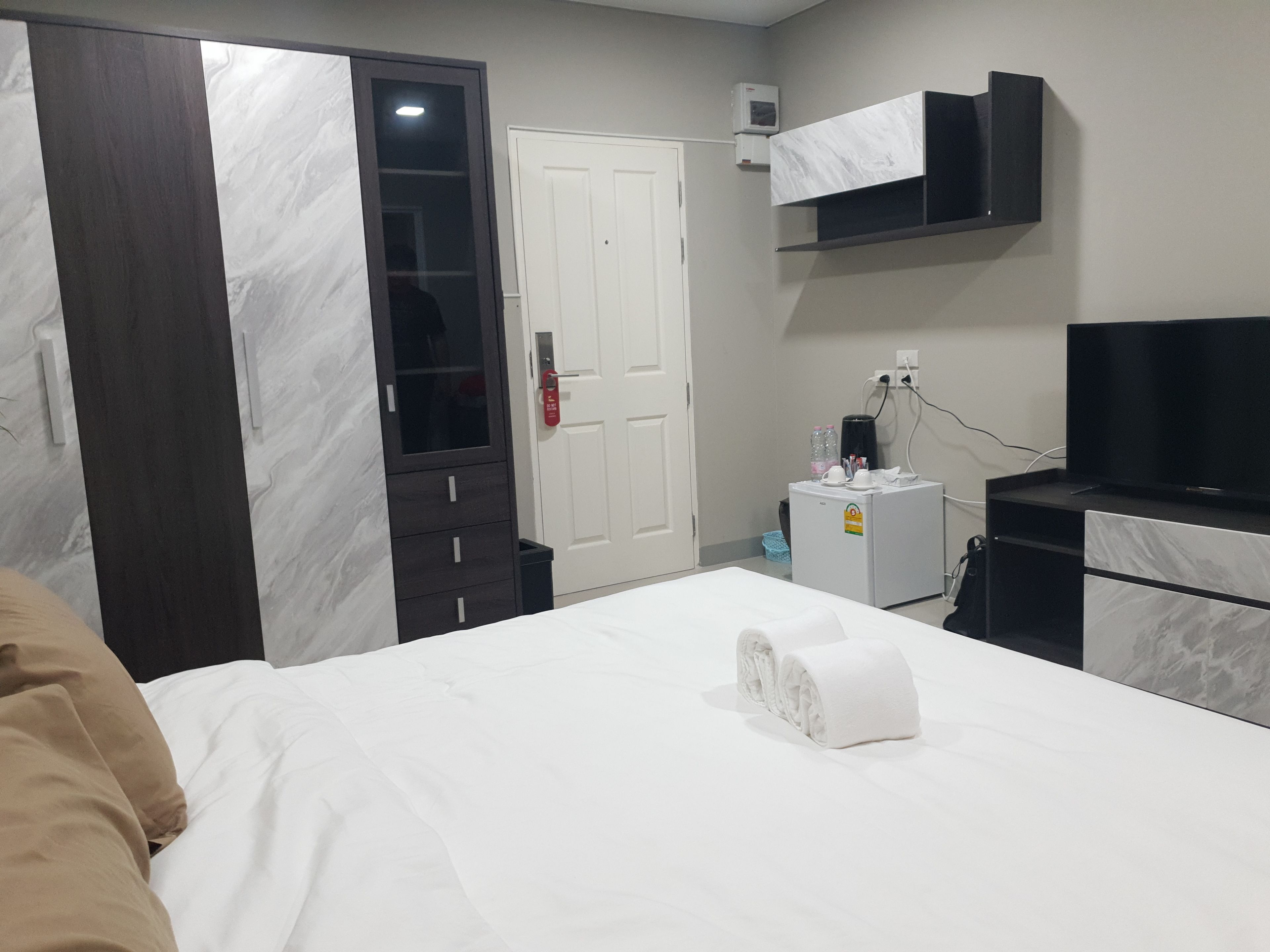 A hotel room with a bed, a wardrobe, a desk with a television, and a minibar.