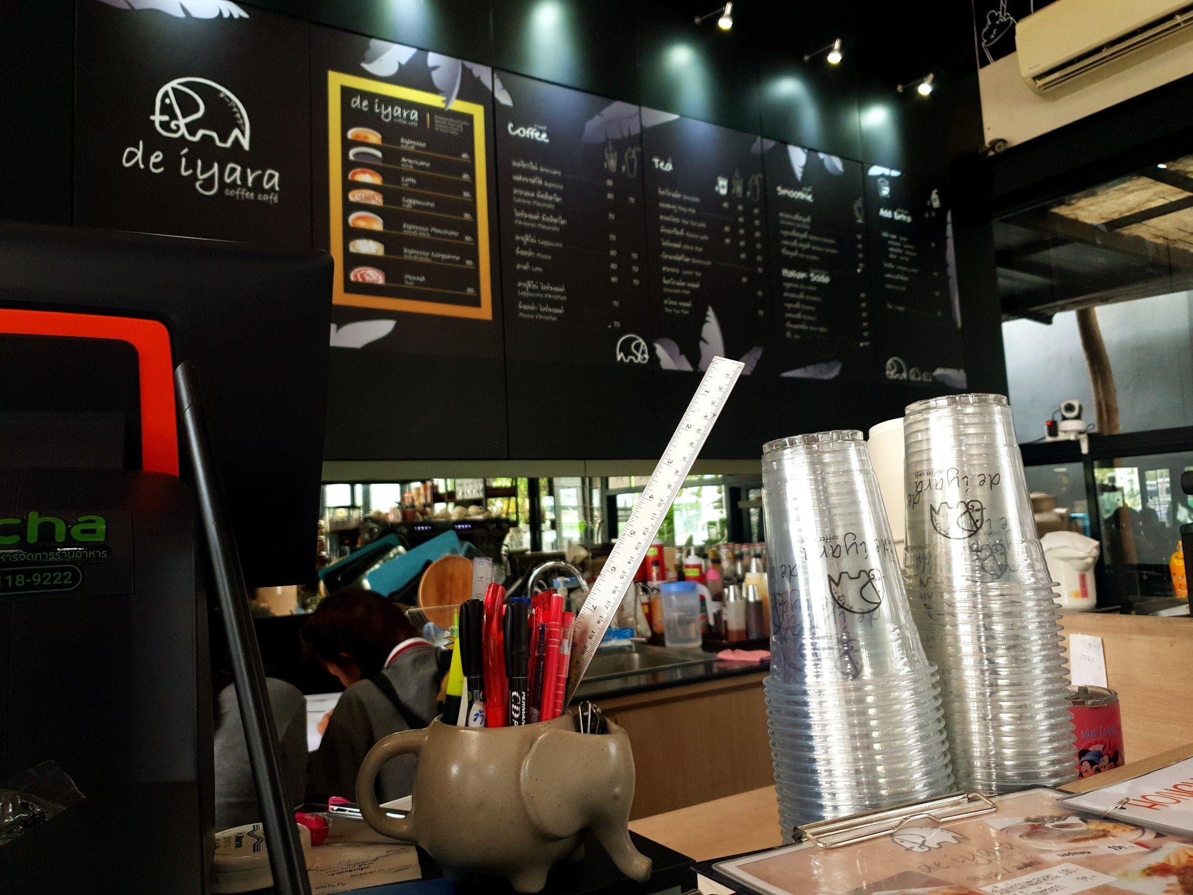 A coffee shop interior with a menu board, a coffee machine, and a counter with stacked cans and a mug.