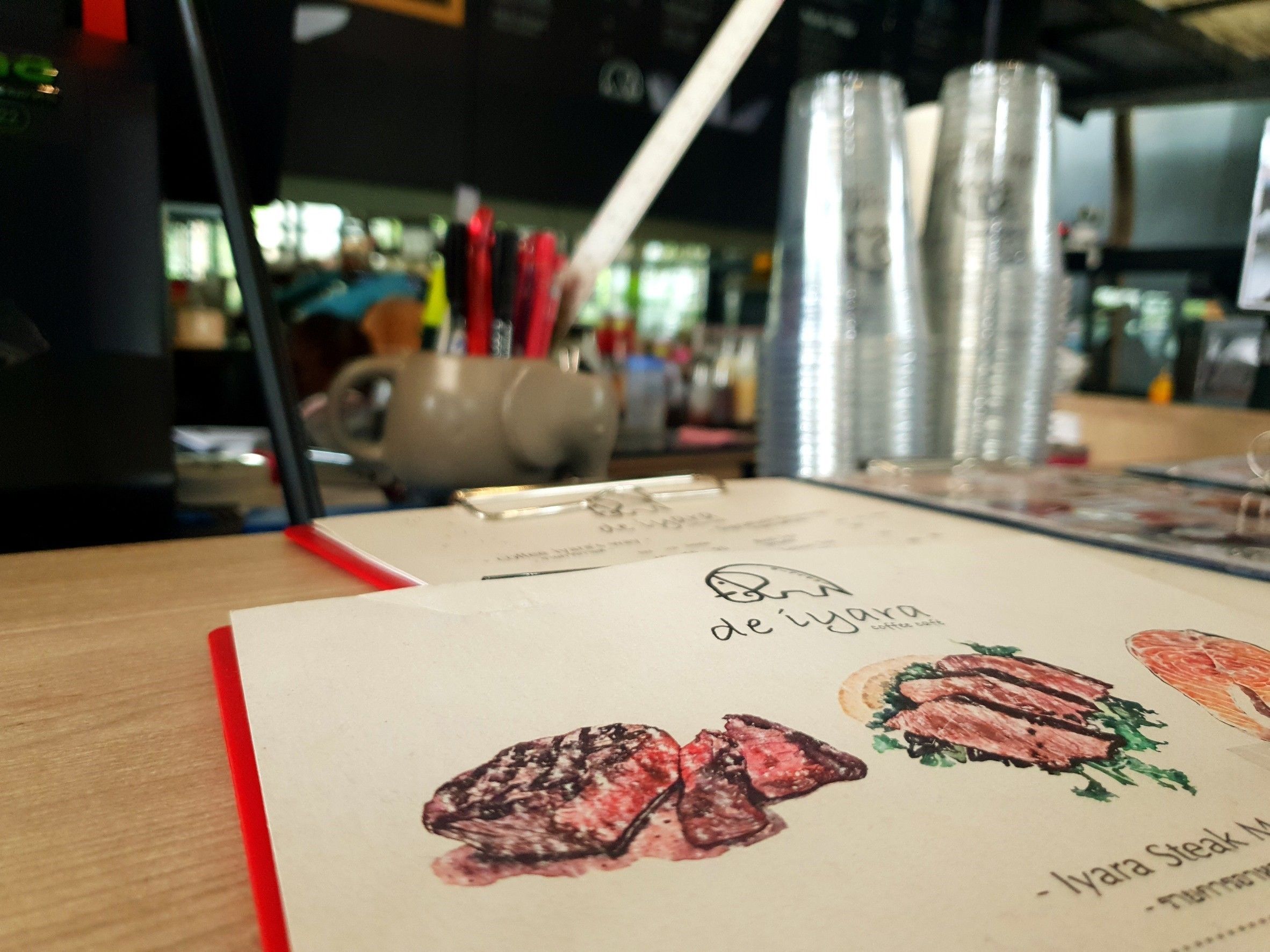 Eine Speisekarte mit Illustrationen von Speisen, einem roten Stift und einer Aktenablage auf einem Tisch.