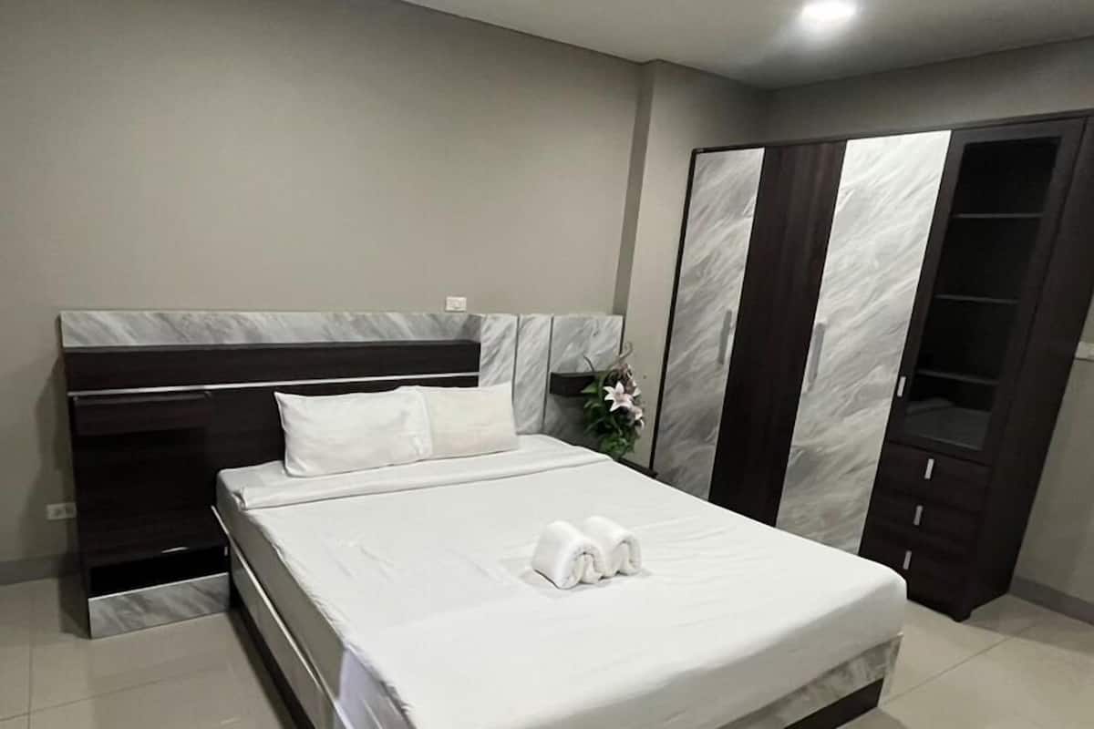 A modern bedroom with a large bed, a dark headboard, a wardrobe, and a mirror cabinet.