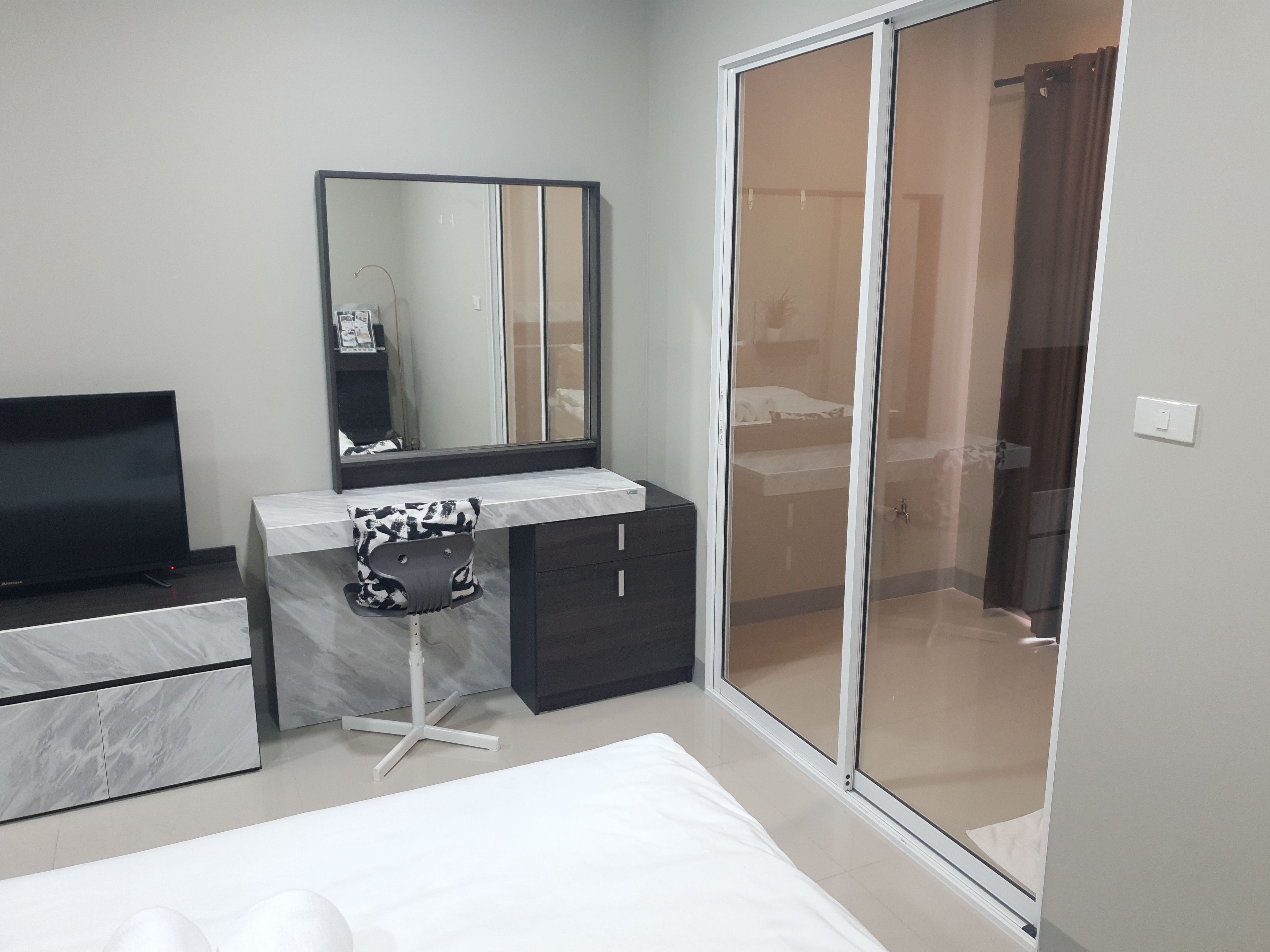 A modern bedroom with a bed, a desk with a chair, a TV, a wardrobe, and a sliding door closet.