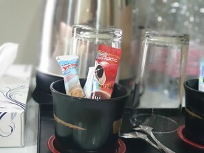 Una taza de café con dos sobres de leche para café y un vaso de agua sobre una mesa.