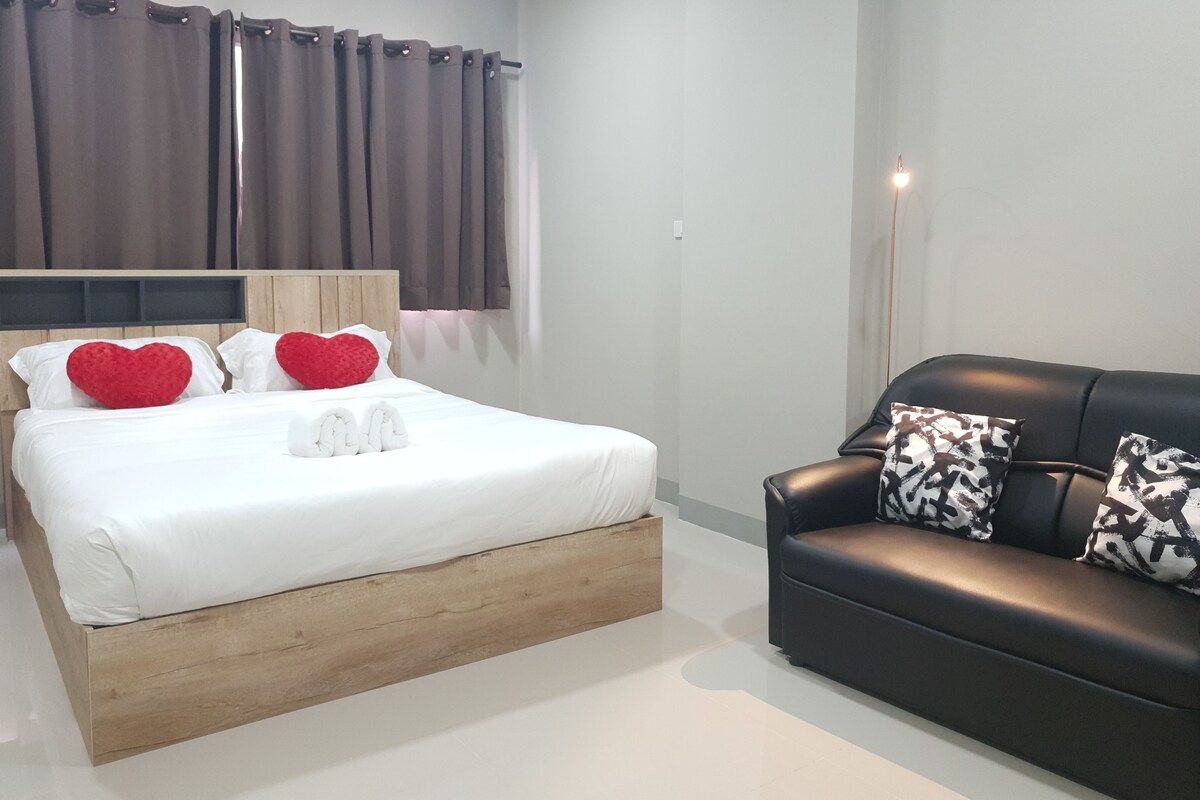 Una habitación de hotel moderna con un cabecero de madera, un sofá de cuero negro y un ventanal con cortinas.