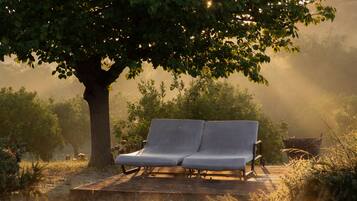 A wooden deck with a bench under a tree, overlooking a pool.