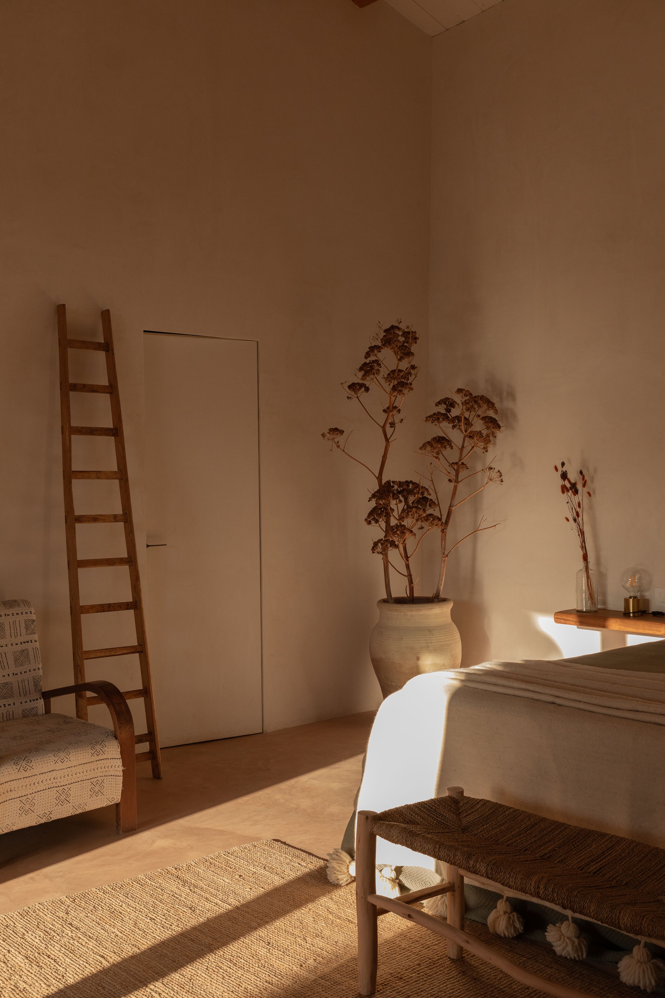 A bedroom with a bed, a wooden ladder, a potted plant, and a bedside table.
