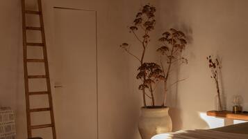 A bedroom with a bed, a wooden ladder, a potted plant, and a bedside table.