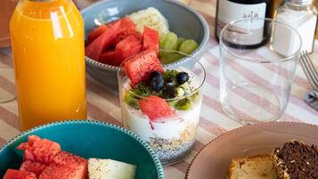 En morgenmadsborddækning med en kande, en skål med frugt, et glas juice og en skive brød på en ternet dug.