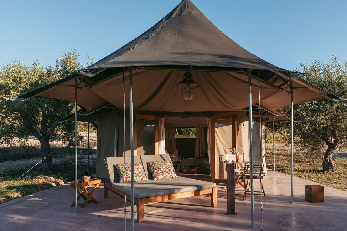 A tented accommodation with a lounge area, a dining setup, and a view of the surrounding landscape.