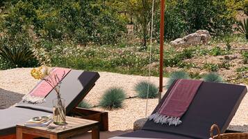 A sunlit outdoor seating area with lounge chairs, a table, and a large umbrella.