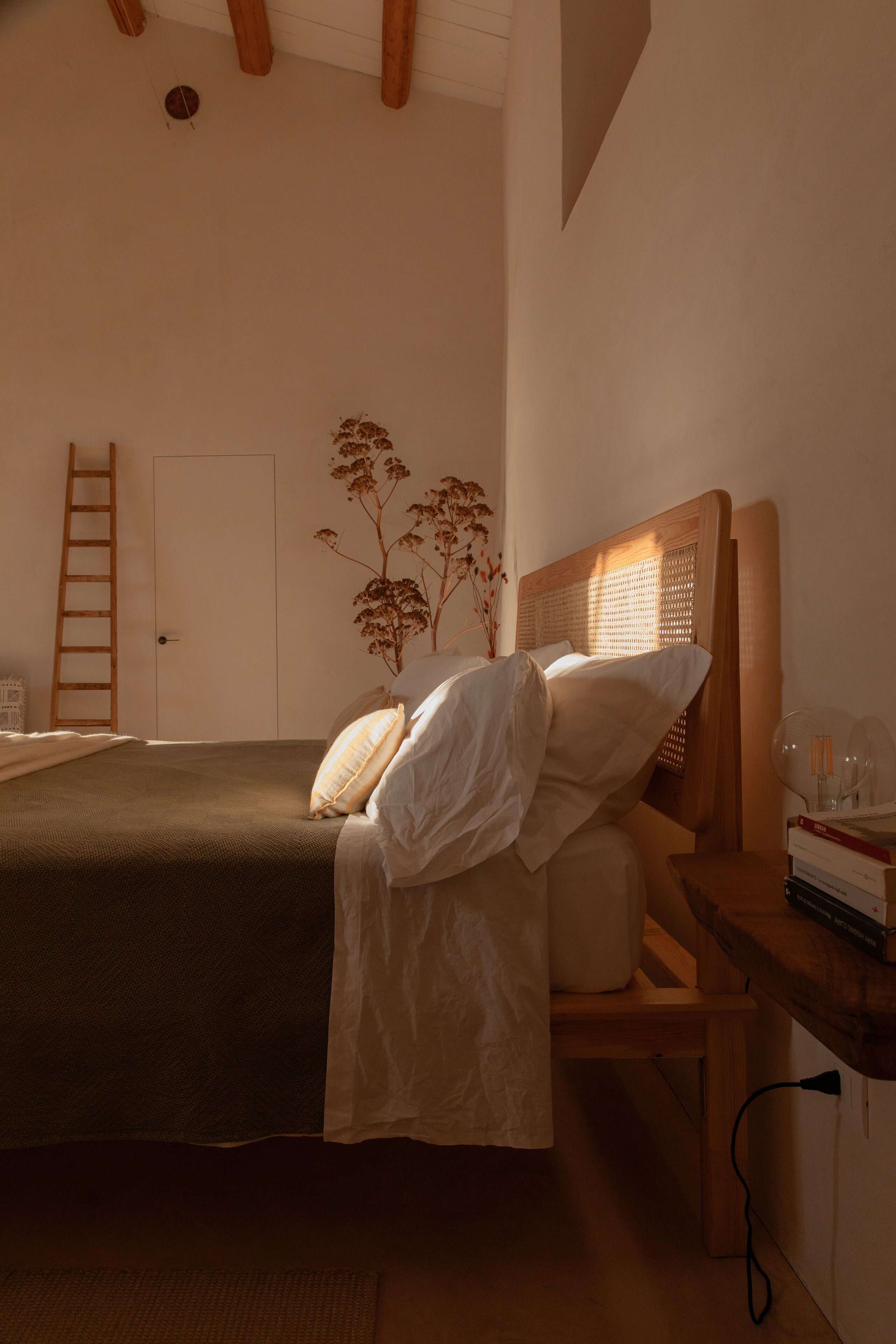 Un dormitorio con una cama, una mesita de noche de madera, una escalera y una puerta.