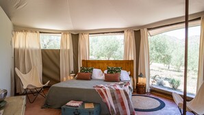 Quarto com cama, cortinas, uma cadeira, uma mala e vista para o exterior.