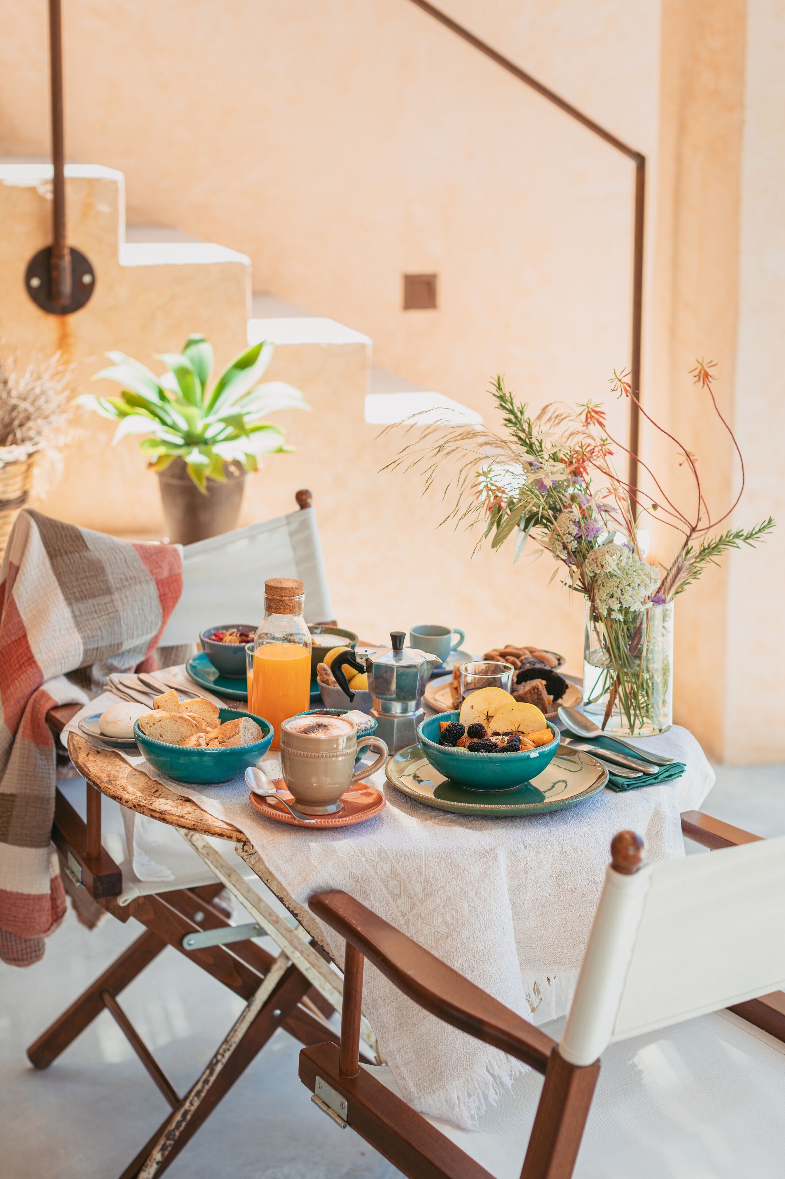 Une table de petit-déjeuner dressée avec des assiettes, des bols et un vase rempli de fleurs.