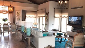 A spacious living room with a large sofa, a dining area with wicker chairs, a fireplace, and a television. - Regnum Golf Country 3 bedroom 4 (Bodrum)